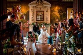 Een pasgetrouwd stel begint te recupereren van hun ceremonie in The Belvedere in Baltimore, MD, terwijl een bloemenmeisje naast hen rent met haar boeket in de hand, terwijl gasten juichen en met kleurrijke slingers in de lucht zwaaien.